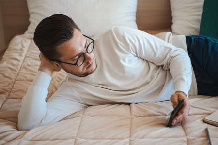 Man is using the smartphone lying on his bed while taking a break from work. Using telephone. Mobile communication.の写真素材