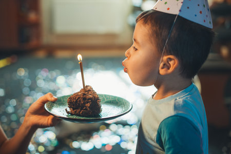 Side view of an four year old kid blowing candles on slice of homemade baked cake. Celebrating birthday. Birthday party for kids.の写真素材