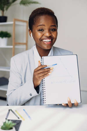 Smiling afro american female teacher showing a blank sheet of paper at camera teaching maths...