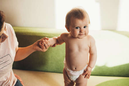 Cute little girl holding mom hand and looking at camera while standing on sofa. People lifestyle concept.の写真素材