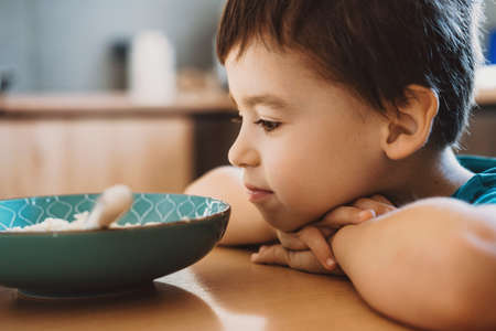 Boy with his head resting on the table and wondering whether to eat the porridge or not.の写真素材