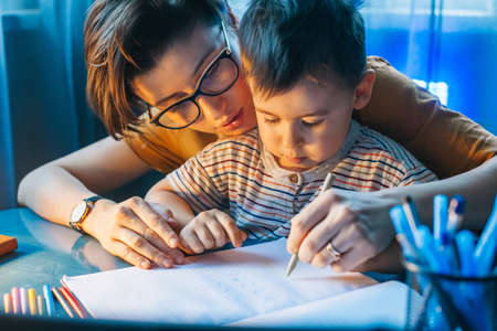 Little boy doing homework at home with school books helped by his mother. For lifestyle design....
