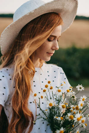 Caucasian woman in hat holding daisies bouquet. Closeup portrait. Natural beauty. Beautiful girl. Spring bouquet. Chamomile flower field. Beauty face. Spring flowers.の写真素材