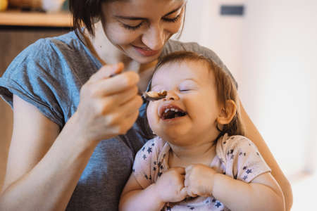 Baby feeding spoon by mother at home. Mom hand feeding baby. Family care. Baby care.の写真素材