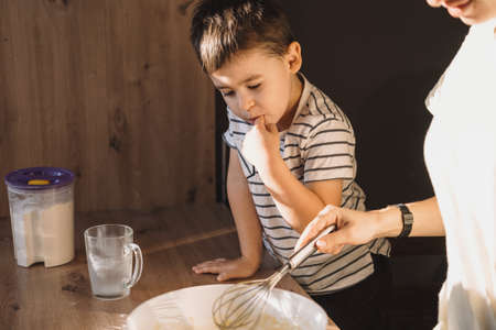 Mothers hands mixing ingredients for dough with son at modern kitchen. Parent helping child. Family weekend.の写真素材