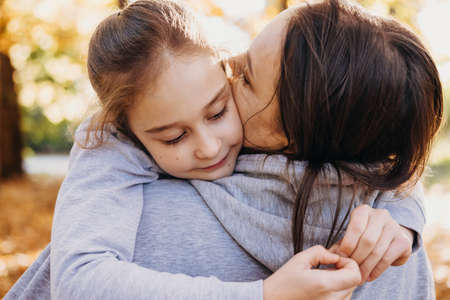 Close-up portrait of a pretty girl lovingly embracing her mother. Portrait of mother daughter fun park. Smiling happy child. Sunny day.の写真素材