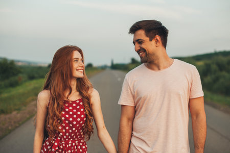 Excited girl and boy having their first date smiling and looking at each other as they walk along the paved road away from people. Front view. Smiling man. Summer vacation.の写真素材