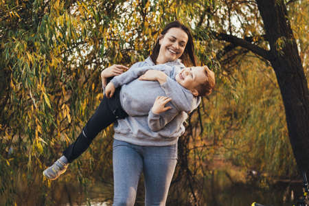 Mom holding her son in her arms in the air while playing an interesting game outside in the park....