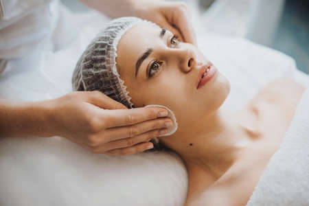 Closeup portrait of a cosmeticians hands washing and cleaning the clients face preparing for peeling procedure. Facial skin treatment. Closeup portrait. Rejuvenation treatment.の写真素材