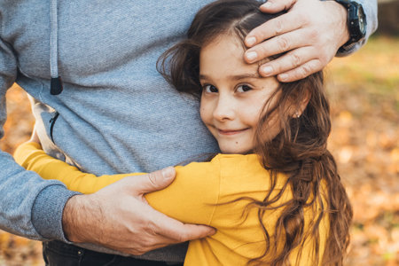 Closeup portrait of a smiling little girl hugging her father outside. Beautiful young girl. Family care. Happy loving family.の写真素材
