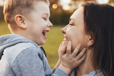 Side view portrait of a happy motherholding her boy on arms outdoors on the nature. Portrait for lifestyle design. Family day. Outdoor fun.の写真素材