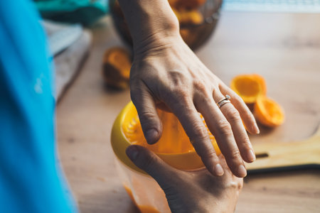 Closeup portrait of womans hands squeezing juice from ripe orange in kitchen. Fresh healthy food. Healthy lifestyle. Natural organic nutrition.の写真素材