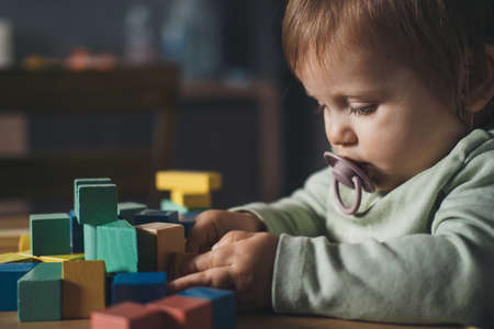 Baby girl playing with colorful toy blocks sitting at table. Building tower of block toys. Children education.の写真素材