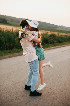 Happy man and woman of lovers kissing and hugging in the middle of the country road. The girl holding a bouquet of daisies. Family day.の写真素材