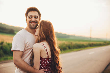 Shot of an affectionate smiling man embracing girlfriend in the middle of the countryroad. Portrait for lifestyle design. Happy family together.の写真素材