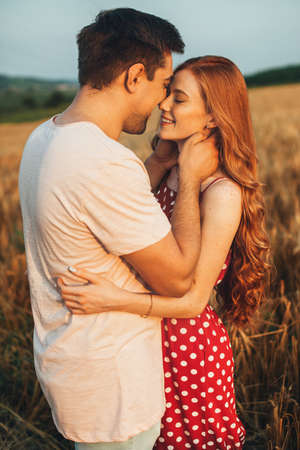 Couple standing close to each other in the wheat field away from the city, following a kiss. Nature...