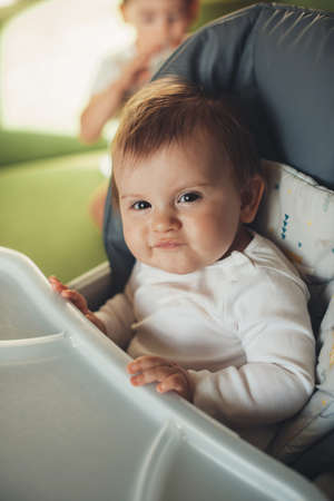 Adorable baby sitting in a high-chair and looking suspiciously at the camera. Facial expressions....