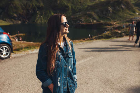 Woman standing in the middle of the road looking at the mountain on which she is going to climb together with the group of other tourists. Summer road trip.の写真素材