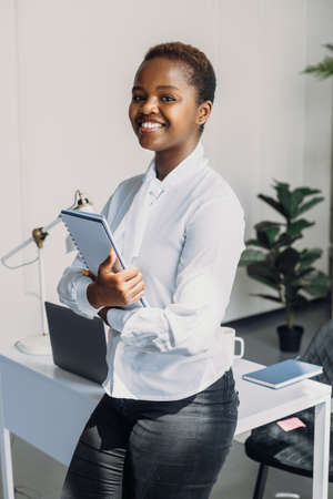 Portrait of african entrepreneur woman holding notebook while standing looking at camera in the...