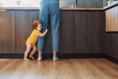 Baby girl standing by mothers legs at home in kitchen. Baby care.の写真素材