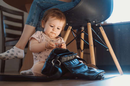 Baby girl sitting on the floor and playing with her mothers bag, taking everything out while mum is...