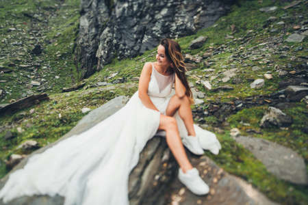 Bride with long hair sitting on a stone against the background of rocks and cliffs, and looking to one side. Fashion model.の写真素材
