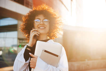 Caucasian businesswoman with curly hair on coffee break talking on phone having conversation with...