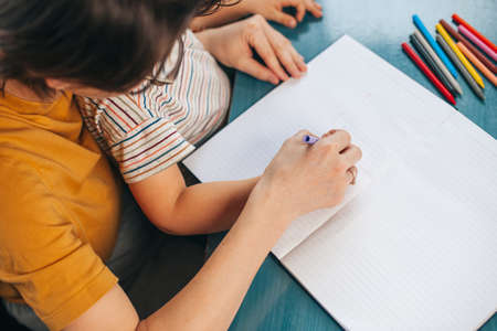 Top view of a mom helping her son kid with homework and exercises. Difficulties with preparation for school and learning write and draw. Family happiness and supportの写真素材