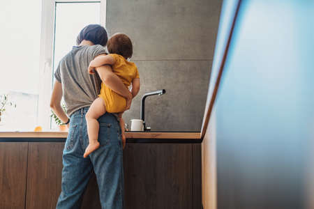 Rear view of mother holding her daughter in the kitchen, cooking together. Motherhood concept. Family concept. Beauty concept.の写真素材