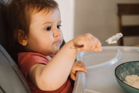 Baby try eating the oatmeal with a spoon from a bowl. Little boy learning to feed herself. Smiling happy child.の写真素材