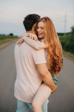Man carrying his ginger girlfriend on shoulder while walking by the country road, the girl laughs. I...