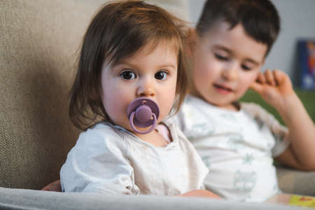 A portrait of two kids sitting on the sofa at home. Family care. Happy family. Baby care.の写真素材