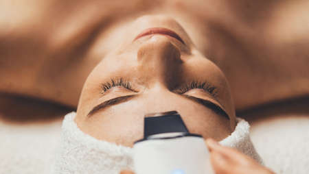 Portrait of woman face with closed eyes getting ultrasonic peeling in spa salon. Skin care. Girl facial treatment. Beauty treatment. Cosmetology. Beauty spa salon.の写真素材
