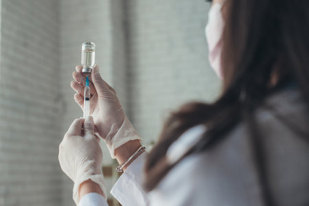 Doctors hands wearing medical glove holding syringe taking covid 19 corona virus liquid vaccine from vial bottle. Covid-19 antiviral vaccine. Coronavirus vaccination. Immunization of citizens.の写真素材