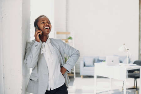 Afro woman entrepreneur smiling while talking on mobile phone standing in the office. Modern communication. Modern technology.の写真素材