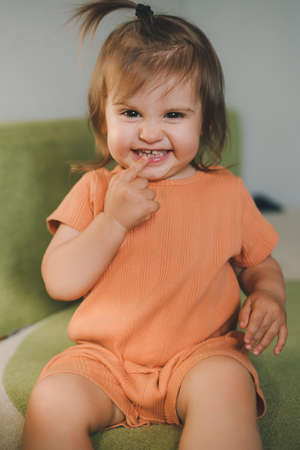 Cute little girl showing to the camera how many teeth she has grown, touching her teeth with her finger and smiling widely. Childhood concept. Funny playful babyの写真素材