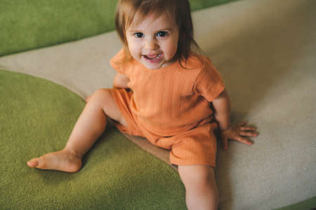 Portrait of a funny little baby girl, smiling looking at the camera sitting on a couch. Happy family. Beautiful young girl.の写真素材