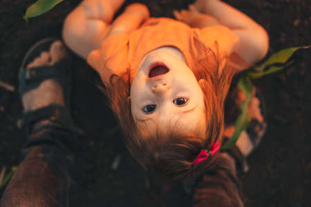 Top view of a girl looking up at the camera while sitting on the cold morning ground in a corn field. Attractive beautiful girl. Smiling happy child.の写真素材