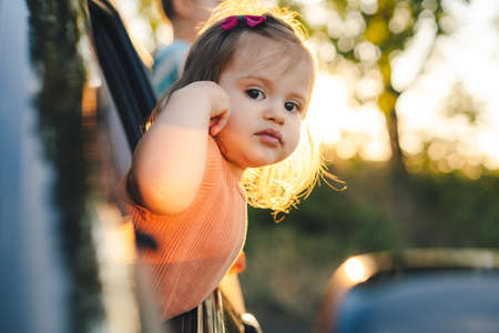 Baby girl peeking out of the car window and smiling while looking at the camera. Happy family. Fresh wind.の写真素材