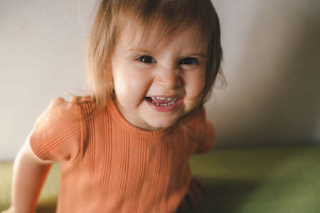 Portrait of little baby girl standing on sofa smile and look at camera enjoying morning weekend in...