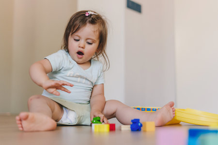 Cute baby girl playing with colorful blocks sitting on a floor at home. Baby development. Educational toys for young children. Construction block for baby or toddler kid.の写真素材
