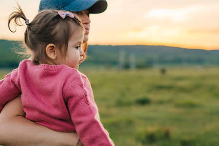 Mother walk across field holding in arms her baby girl. Family outdoor recreation. Portrait mom with child together in nature.の写真素材