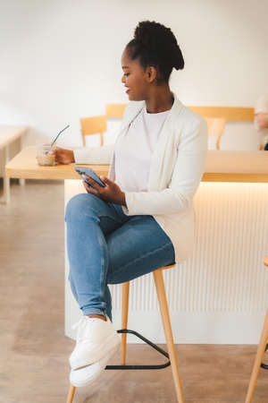 African businesswoman chatting with friends while serves her coffee during break, at cafe. Message notification. Communication concept.の写真素材