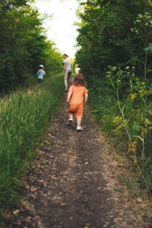 Family of three walking down the road. Happy family outdoors. Back view. Green grass field. Active travel.の写真素材