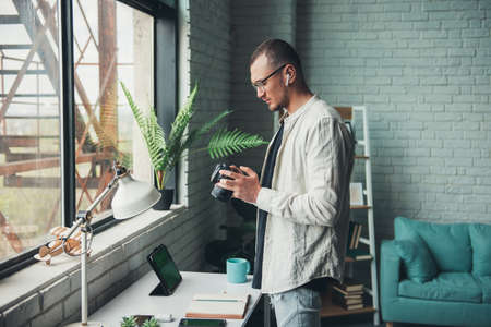 Side view of a photographer holding camera in the hand and looking at the pictures. Photo shooting. Studio fashion portrait. Professional studio photography.の写真素材