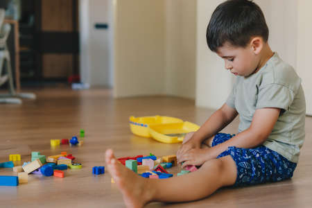 Concentrated boy playing toys sitting on warm floor in modern living room. Baby development. Small house.の写真素材