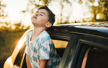 Portrait of child boy sticking his head out the car window. Concept of road trip. Summer nature. Road trip. Kid life.の写真素材