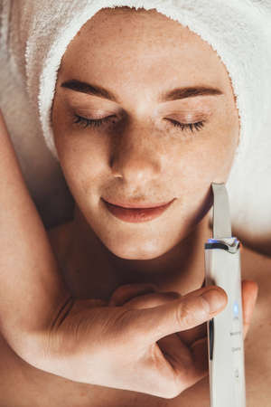 Close-up portrait of woman face receiving ultrasound cavitation facial peeling. Spa treatment. Beauty woman face skin care. Hardware cosmetology.の写真素材