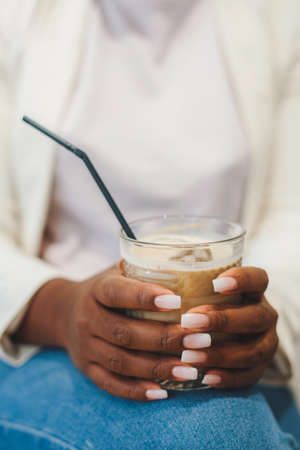 Afro womans hands holding glass cup of iced coffee. Coffee time in summer day. Morning mood.の写真素材