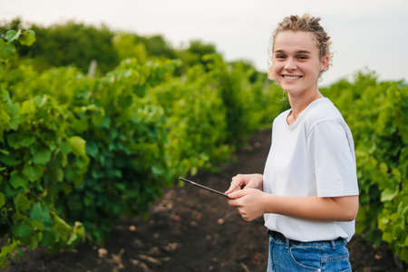 Farmer with a tablet standing in plantation of grapevines, smiling looking at camera, enjoying work time. Free space for text. Smart farming and precision agriculture by integrating technology.の写真素材